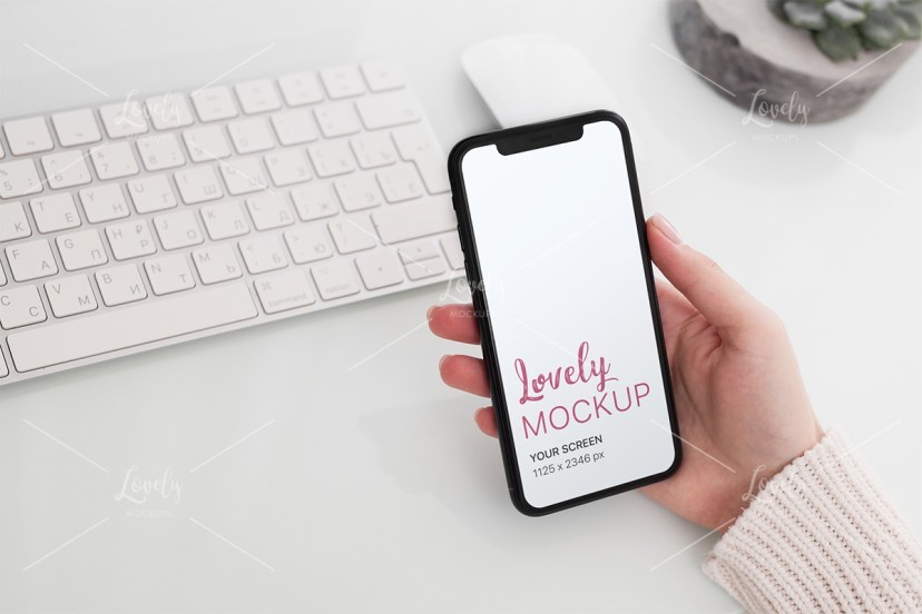 mockup and womans hand holding an iphone 11 over a desk